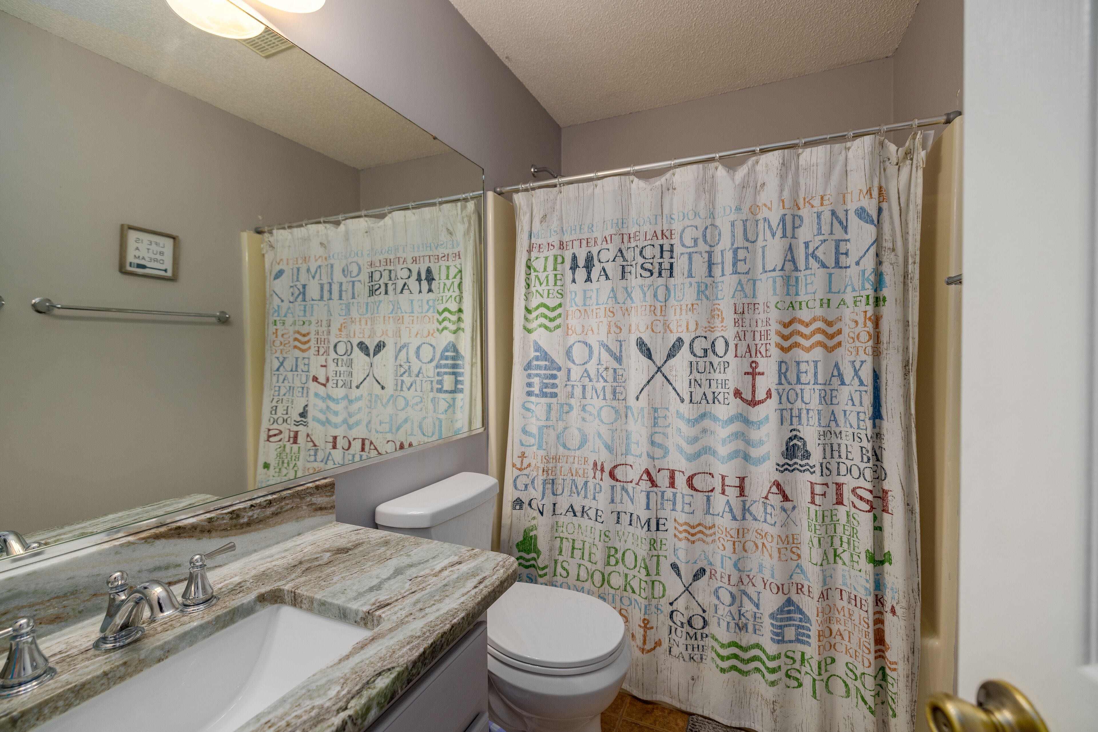 A bathroom with a marble sink, a toilet, and a shower curtain with nautical-themed text.