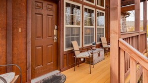 A wooden porch with a door, two windows, and a small table with chairs. - Bear Hug (Reeds Spring)