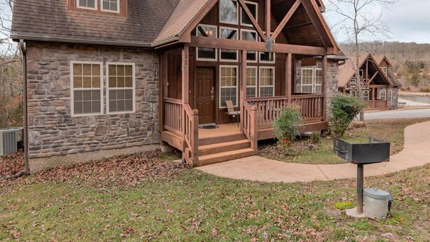 A stone and wood lodge with a large porch, multiple windows, and a mailbox. - Bear Hug (Reeds Spring)
