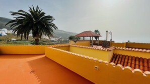 Eine Terrasse mit gelbem Dach, einer Palme und einem kleinen Pavillon.