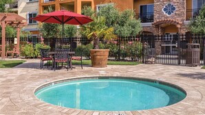 Una piscina con una sombrilla roja, rodeada de mobiliario de exterior y un muro de piedra.