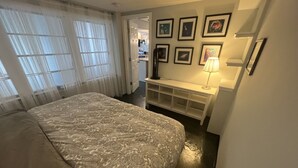 A bedroom with a large bed, a desk with a lamp, and framed pictures on the wall. - Unique Style Apartment STR# 22-0167 (Asbury Park)