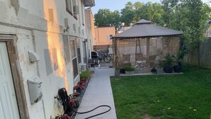 A backyard with a concrete pathway, a gazebo, and potted plants. - Unique Style Apartment STR# 22-0167 (Asbury Park)