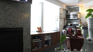 A kitchen with a tiled backsplash, a microwave, a stove, and a sink. There is a window providing natural light, and a potted plant on the counter. - Unique Style Apartment STR# 22-0167 (Asbury Park)