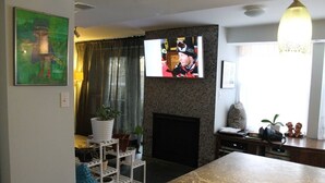 A living room with a fireplace, a television mounted above it, and a dining area with a marble table. - Unique Style Apartment STR# 22-0167 (Asbury Park)