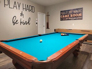 A pool table with a blue felt surface, a cue stick, and a pool ball. There is a sign on the wall that reads "FEELS LIKE MAGIC GAME ROOM". - Exceptional Villa: Saltwater Pool, No Rear Neighbors, Game Room & Movie Theater (Davenport)