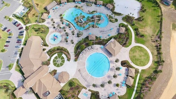 An aerial view of a resort with multiple swimming pools, a central water feature, and a parking lot. - Exceptional Villa: Saltwater Pool, No Rear Neighbors, Game Room & Movie Theater (Davenport)