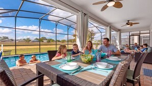 A covered outdoor dining area with a pool, wicker furniture, and ceiling fans. - Exceptional Villa: Saltwater Pool, No Rear Neighbors, Game Room & Movie Theater (Davenport)