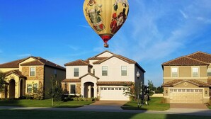 A residential area with a large house featuring a garage, a well-maintained lawn, and a hot air balloon in the background. - Exceptional Villa: Saltwater Pool, No Rear Neighbors, Game Room & Movie Theater (Davenport)