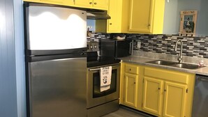 Une cuisine avec des meubles de couleur jaune, un réfrigérateur en acier inoxydable, un four à micro-ondes et une cuisinière.