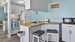 A compact kitchen with white cabinets, a wooden countertop, and a built-in microwave. - Direct Oceanfront condo- AMAZING VIEWS & GREAT AMENITIES! (Ocean City)