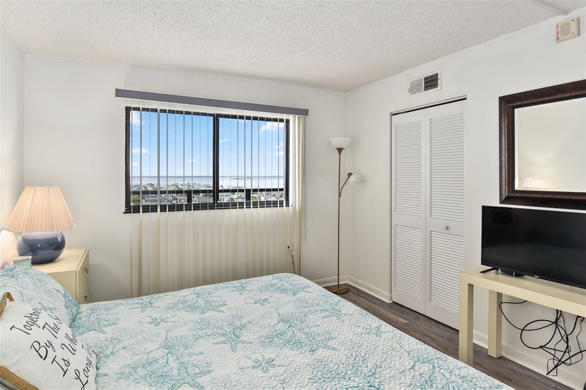 Ein Schlafzimmer mit Bett, Fernseher, Lampe, einem Fenster mit Jalousien und einem Schrank.