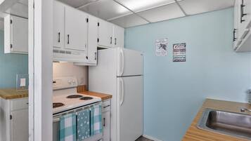 Pieni, käytännöllinen keittiö, jossa on valkoiset kaapit, valkoinen jääkaappi, liesi ja pesuallas.