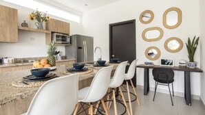 Cocina moderna con encimera de granito, sillas blancas y zona de comedor con una computadora portátil y espejos decorativos.