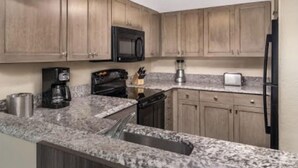 A kitchen with granite countertops, wooden cabinets, a black microwave, a coffee maker, a toaster, and a refrigerator. - June 15-22!  Price reduced! 1 bedroom, Peaceful Beachfront, Westwinds (North Myrtle Beach)