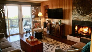 Una sala de estar con chimenea, televisor y puerta corrediza de vidrio que da a un balcón.