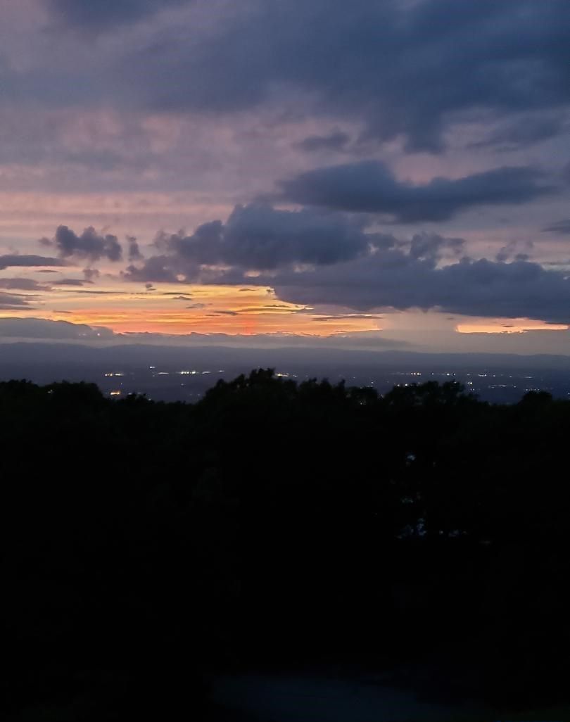 A sunset over a cityscape with visible buildings and a cloudy sky.