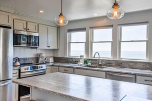 A modern kitchen with stainless steel appliances, a marble countertop, and large windows offering a view.
