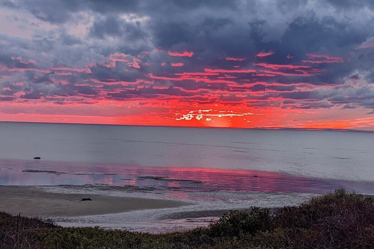 A sunset over a calm sea with a beach in the foreground.