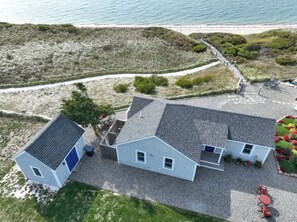 A coastal property with a gravel driveway, a small garden with red flowers, and a view of the beach. - Beachfront on Private Beach w/ AC! (Truro)
