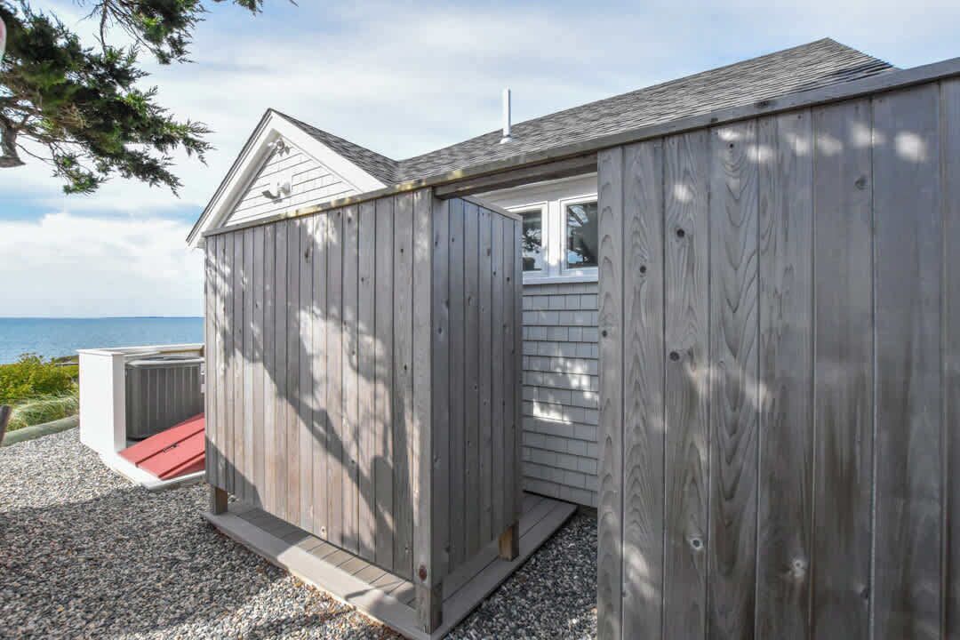 A wooden cabin with a red door, a small porch, and a view of the sea.