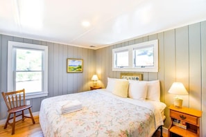A bedroom with a bed, two bedside lamps, a chair, and a window with blinds. - Beachfront on Private Beach w/ AC! (Truro)