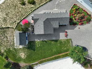 An aerial view of a building with a sloped roof, a parking area, and a landscaped garden with various plants and flowers. - Beachfront on Private Beach w/ AC! (Truro)