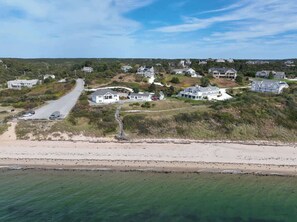 An aerial view of a coastal residential area with houses, a beach, and a road leading to the water.