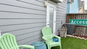 Two green Adirondack chairs, a round blue and white woven stool, and a green sign with the word "Access" on a residential property with a white door and grey siding. - Seas the day! Freshly updated 3/2 with ability to sleep 10 available! (Port Aransas)