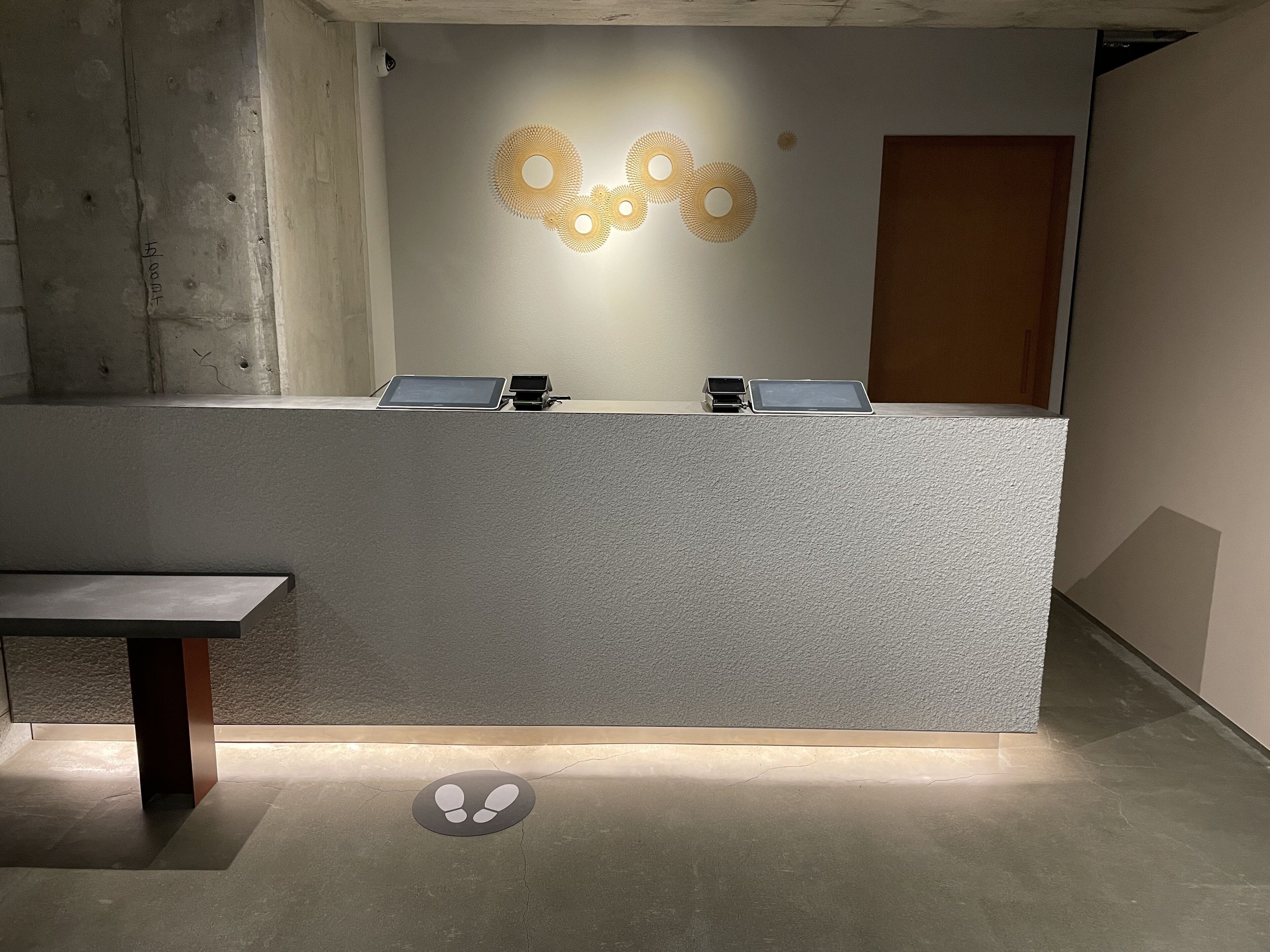 A reception desk with a tablet and a phone, a bench, and a wall-mounted light fixture.