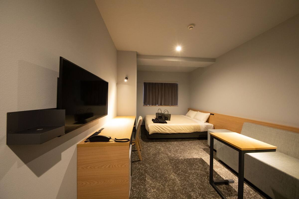 A hotel room with a bed, a sofa, a TV mounted on the wall, a desk, and a small table.
