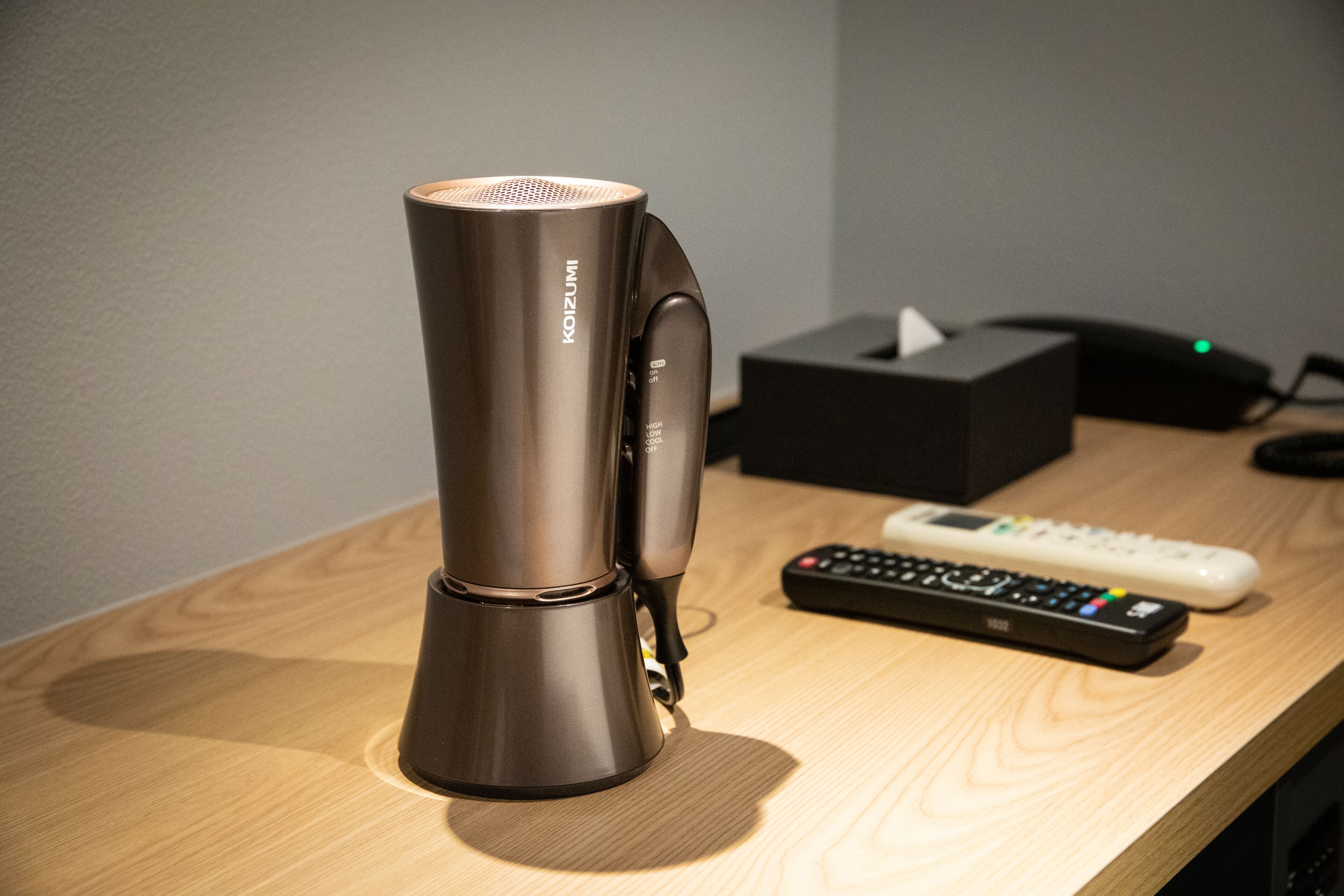 A modern, metallic coffee maker on a wooden table with a remote control and a tissue box nearby.