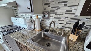 Una cocina con un lavamanos de acero inoxidable, encimera de granito y cafetera.