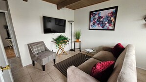 Una sala de estar con un sofá, una butaca, un televisor, una planta y un cuadro en la pared.