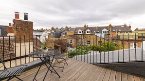 Eine Terrasse mit Tisch und Stühlen, einem Blumentopf und Blick auf Wohnhäuser.