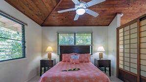 Un dormitorio con techo de madera, una cama con colcha rosa, dos mesitas de noche con lámparas y una puerta corredera tipo shoji.