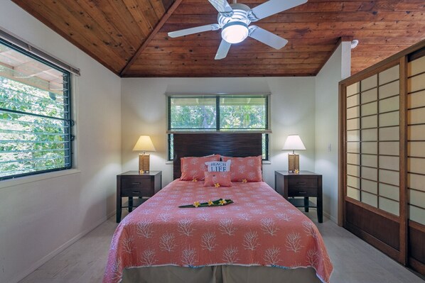 A bedroom with a wooden ceiling, a bed with a pink bedspread, two bedside tables with lamps, and a shoji screen door.