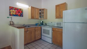 Una cocina compacta con armarios de madera, un refrigerador blanco, una estufa, un microondas y una cafetera.
