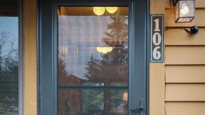 Eine dunkelgrüne Haustür mit Fensterteil, einer Türschild mit der Nummer 106 und einer an der Wand befestigten Laterne.