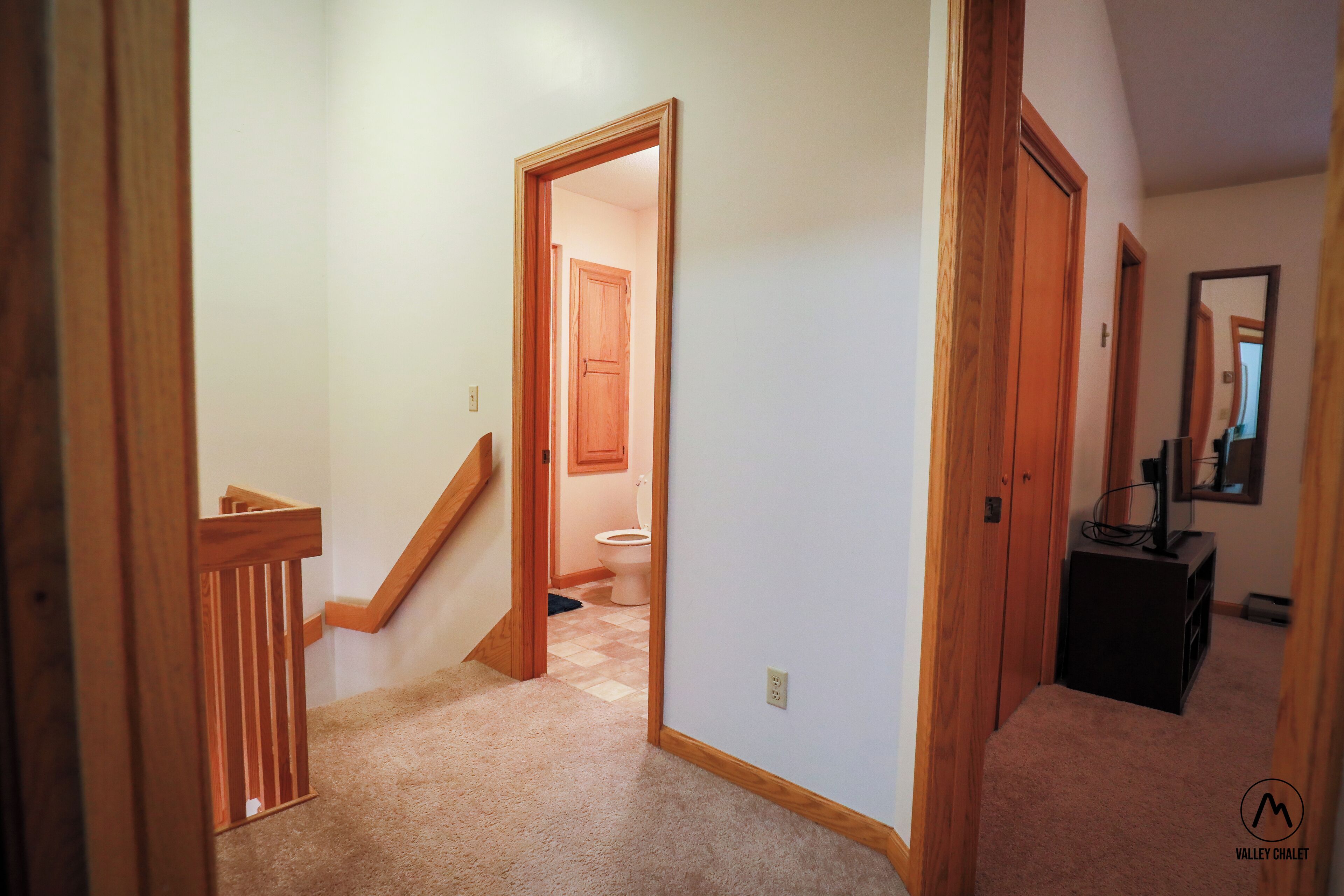 A hallway with carpeted floors, wooden doors, and a staircase leading to another room.