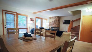 Ein Essbereich mit Holztisch und -stühlen, einem Steinkamin und einer Treppe, die eine weitere Ebene hinaufführt.
