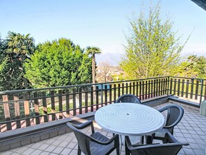 Ein Balkon mit rundem Tisch und Stühlen, einem Metallgeländer und Blick auf Bäume und Berge.