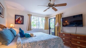 Ein Schlafzimmer mit Bett, Deckenventilator, Fernseher und einem Fenster mit Vorhängen.