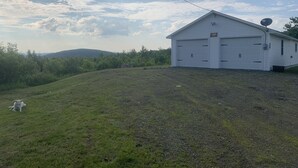A white single-story building with a garage, surrounded by a grassy hill and trees.
