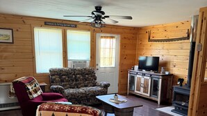 A cozy living room with wooden walls, a ceiling fan, a fireplace, and a television.