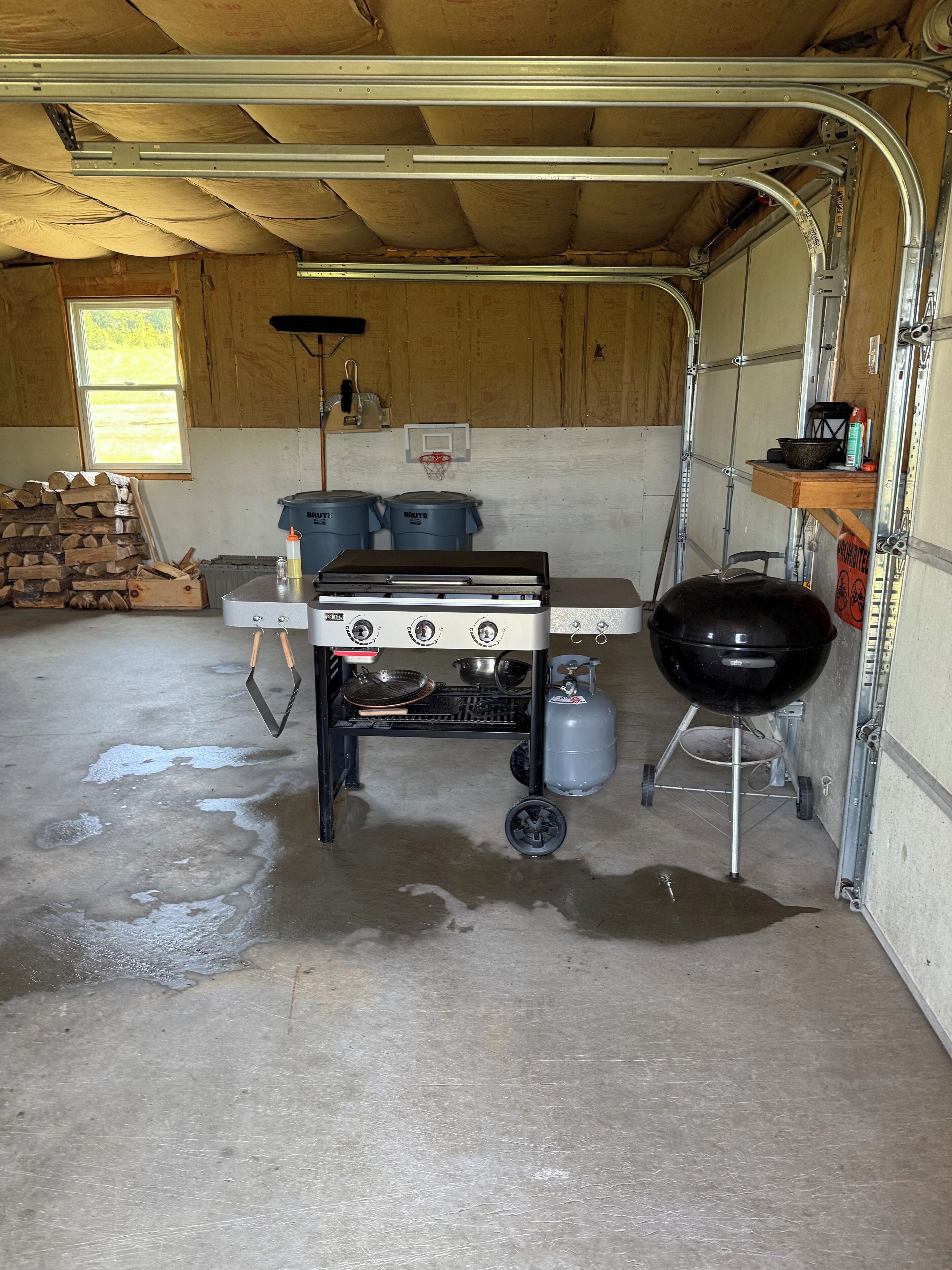 Garatge amb una cuina de gas portàtil, una barbacoa i una pila de llenya.