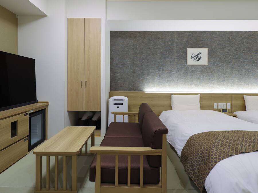 Una habitación de hotel con cama, sofá, televisión, una mesita y un armario.