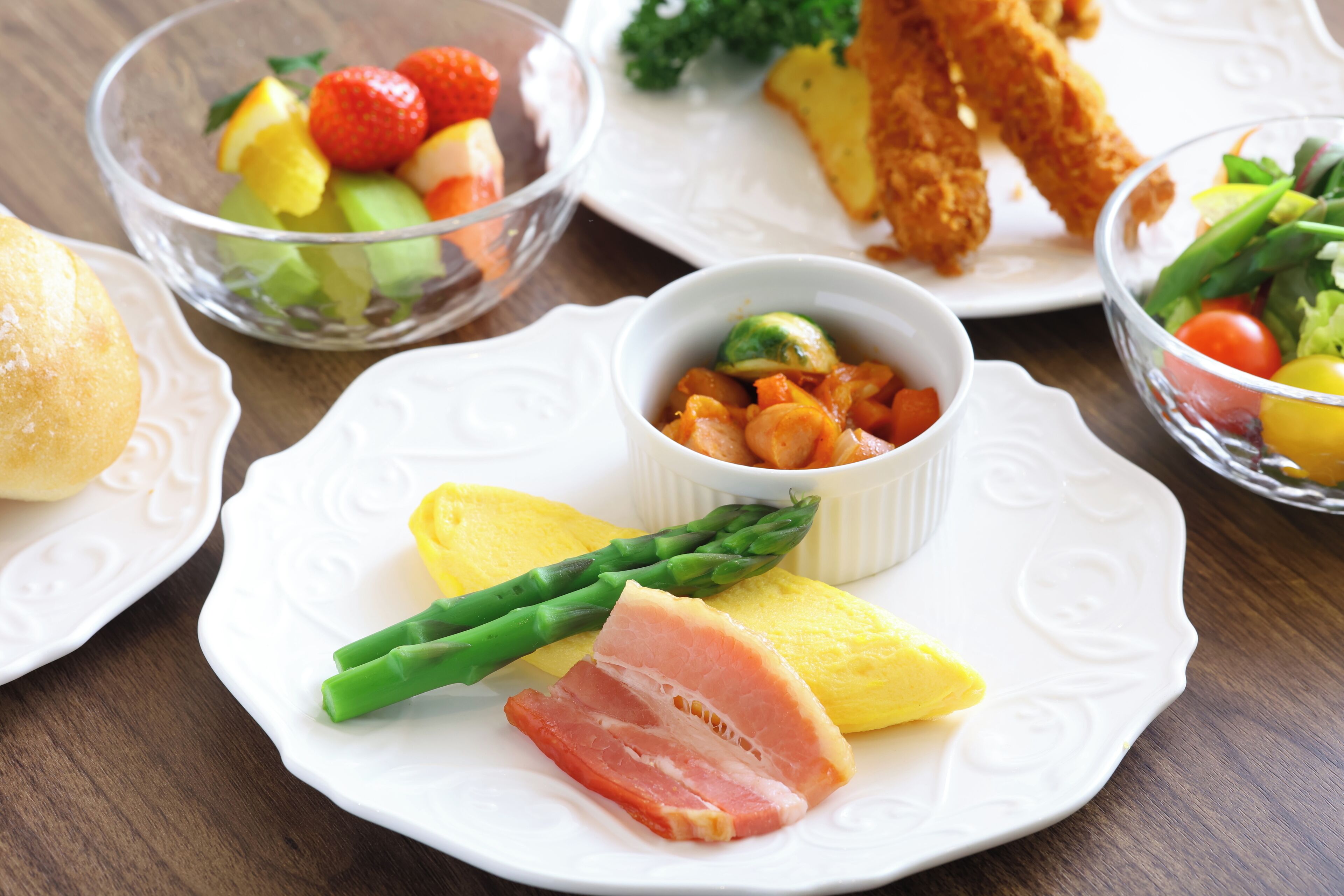 A table with various dishes including asparagus, ham, and a fruit salad.