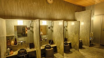 Casa de banho pública com vários espaços, um relógio na parede e um contentor de lixo em cada espaço.
