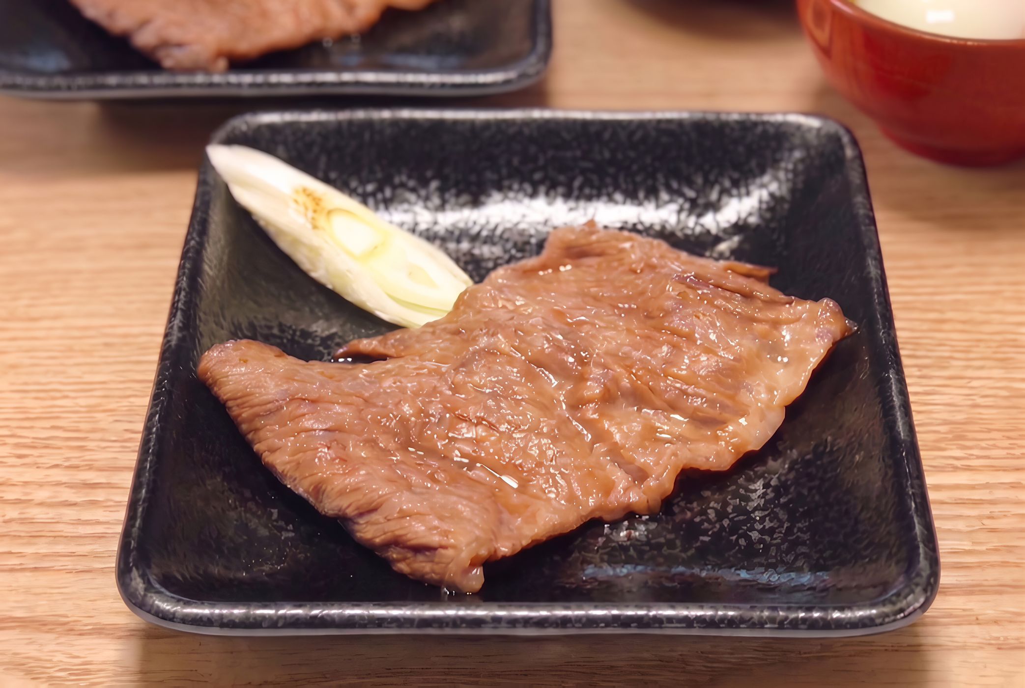 Une assiette en céramique noire sur laquelle on voit un morceau de viande cuite et un œuf dur, le tout posé sur une table en bois.